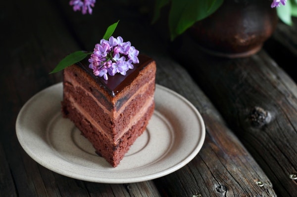 Tallerken med et stykke chokoladekage med spiselige blomster - blålilla syren - på toppen. 